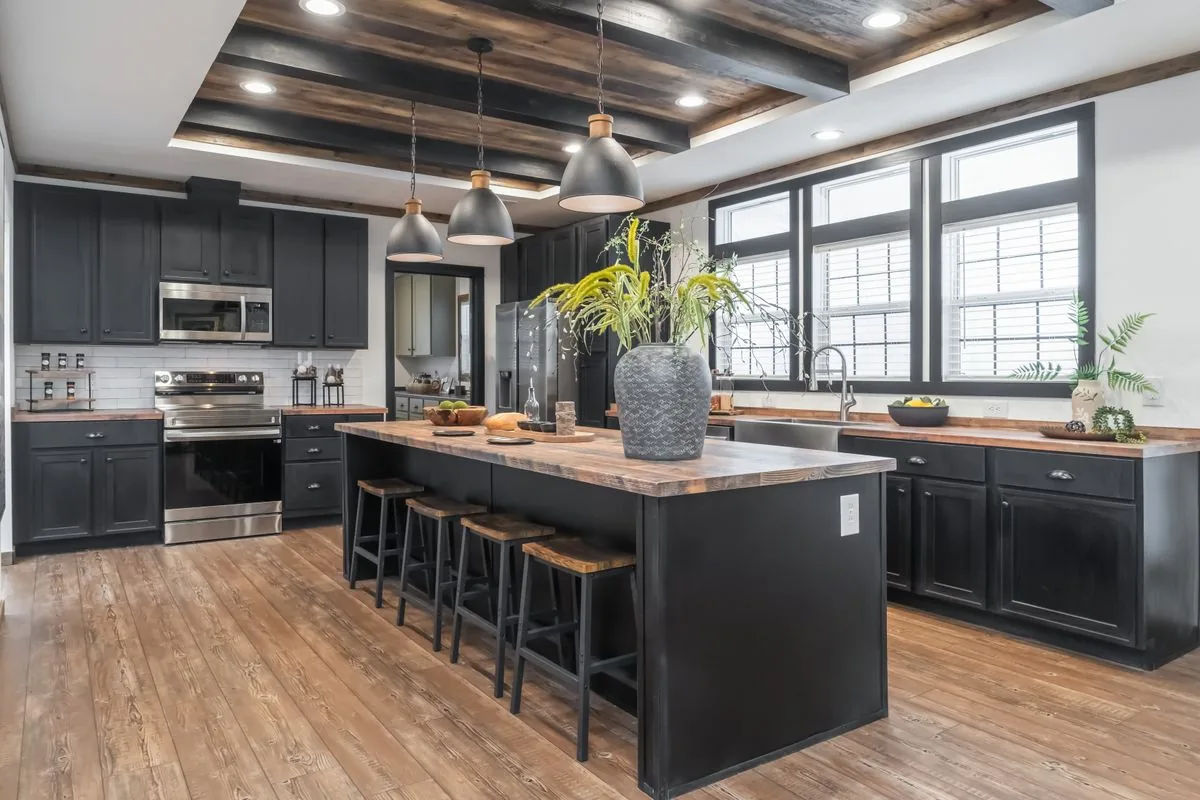 Model home kitchen with dark cabinets, wood beam ceiling and a large island with bar stools