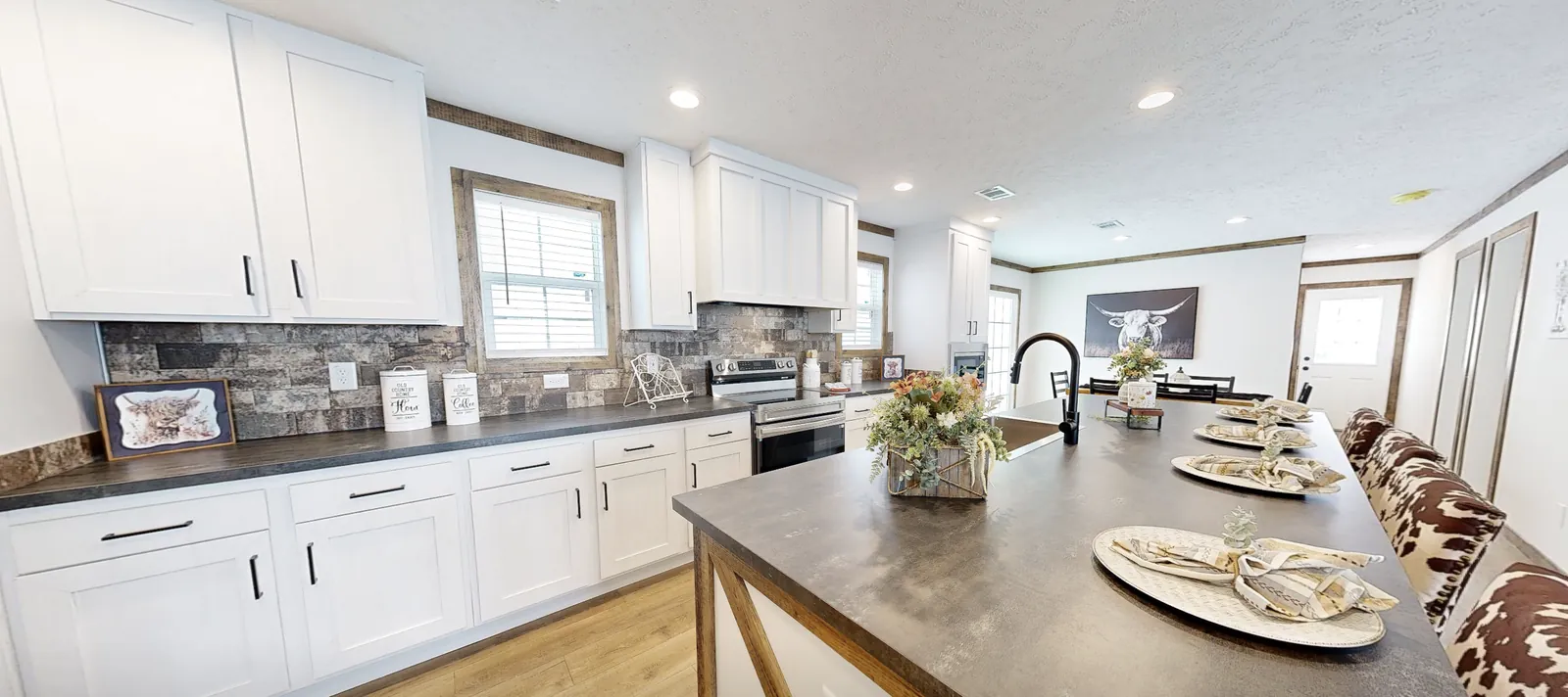 Long white kitchen with stone-look backsplash, dark countertops and an island set for dinner